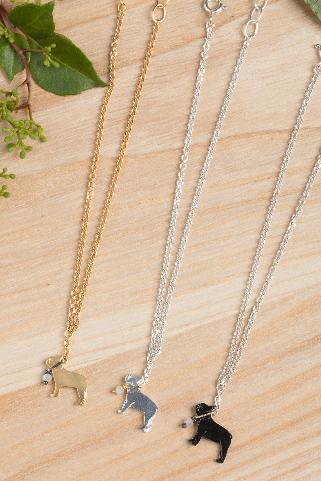 Gold, silver, and black french bulldog necklaces on a wooden countertop