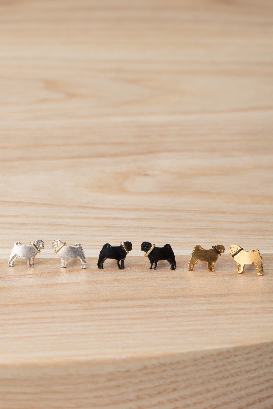 Three pairs of tiny pug stud earrings in silver, black ruthenium, and gold respectively. 