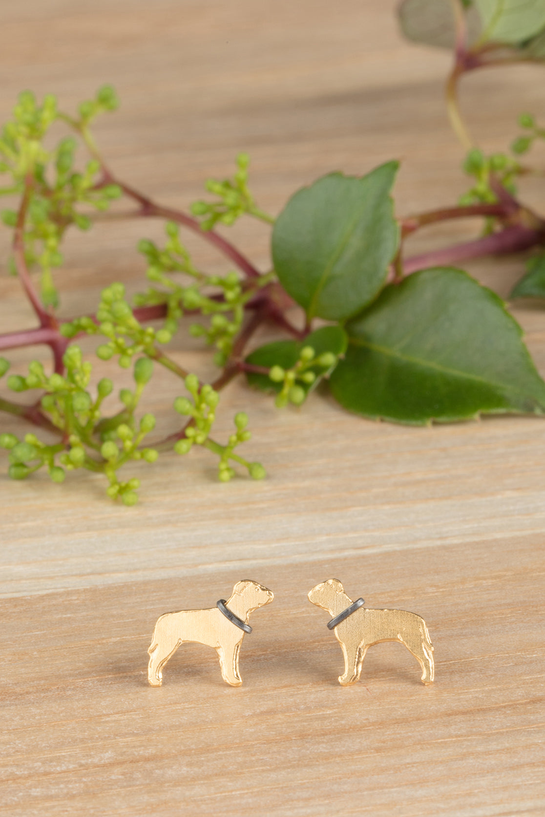 Handmade 22ct gold dog earrings on a wooden surface